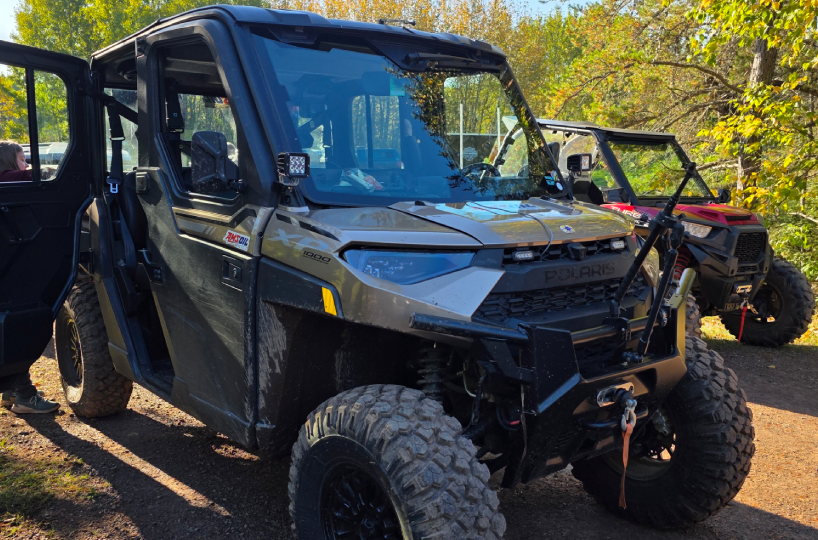 Black off-road vehicle parked in a wooded area with a person in the background.